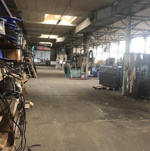 Geräumige Lagerhalle mit Betonboden, hohen Decken und sichtbaren Stahlträgern, gefüllt mit Arbeitsmaterialien und Geräten.