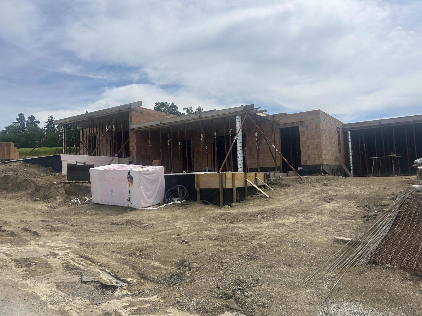Rohbau eines Hauses mit Ziegelwänden und Holzstützen für die Deckenkonstruktion auf einer Baustelle.