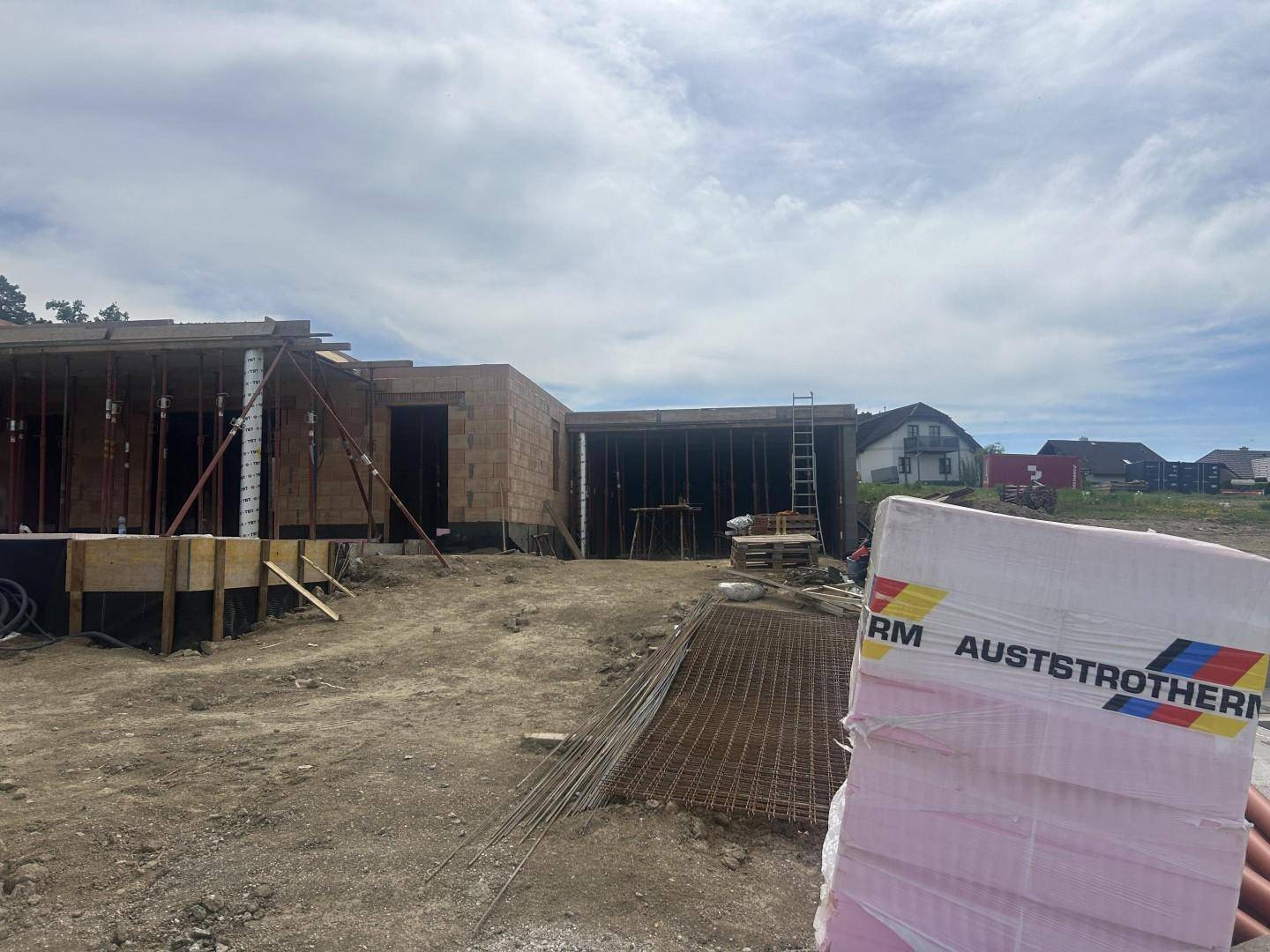 Rohbau eines Hauses mit Ziegelwänden und Dämmmaterial im Vordergrund auf einer Baustelle.