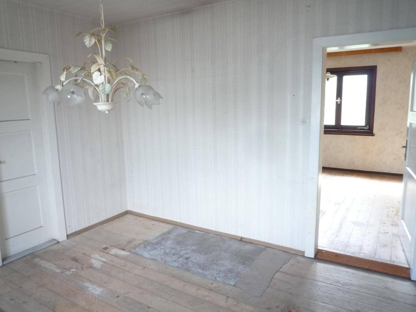 Leerer Raum mit Holzdielenboden und weißer Tür, der in einen weiteren Raum führt.
