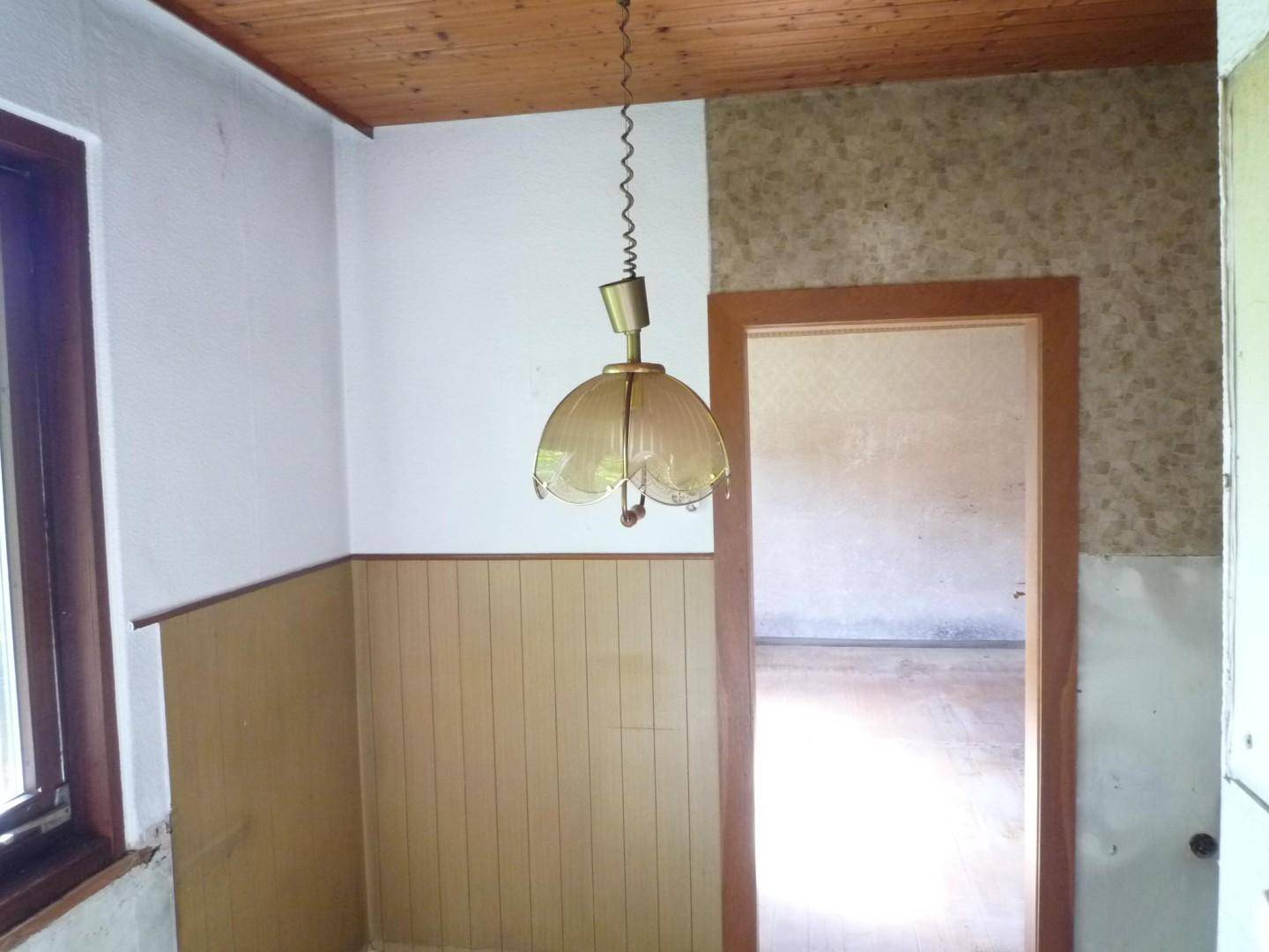 Raum mit Holzdecke und Holzvertäfelung, einem Fenster und einer altmodischen Deckenleuchte.