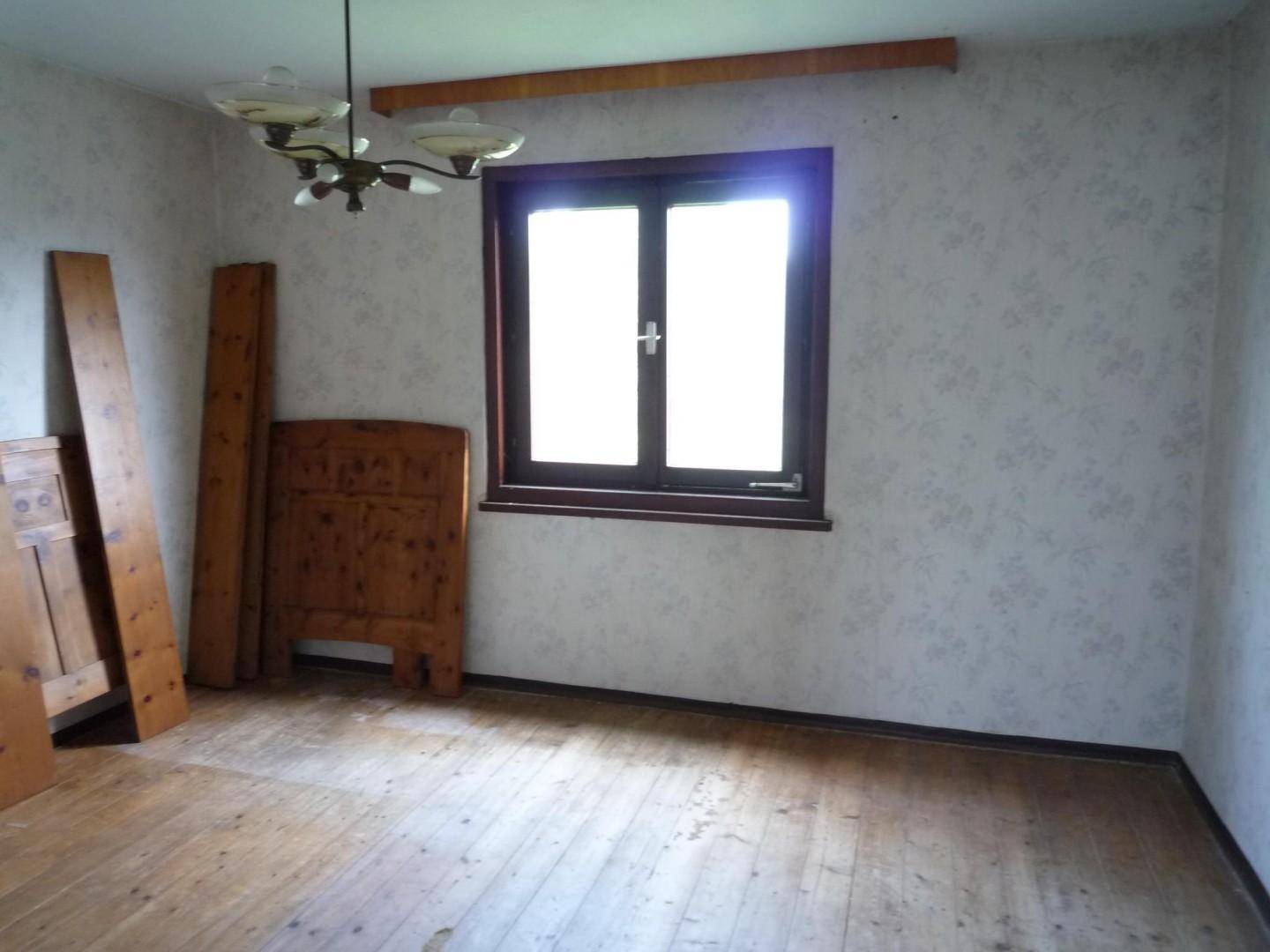 Leerer Raum mit Holzdielenboden, einem Fenster und einer einfachen Deckenleuchte.