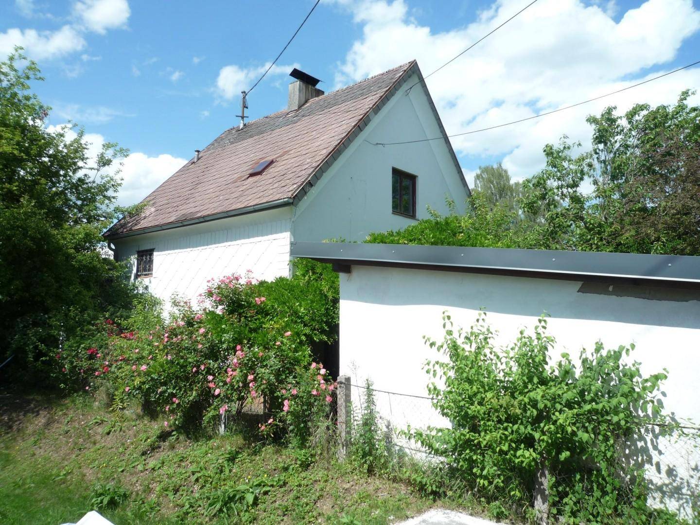 Rückseite des Hauses mit blühenden Rosenbüschen und einem kleinen Nebengebäude im Garten.