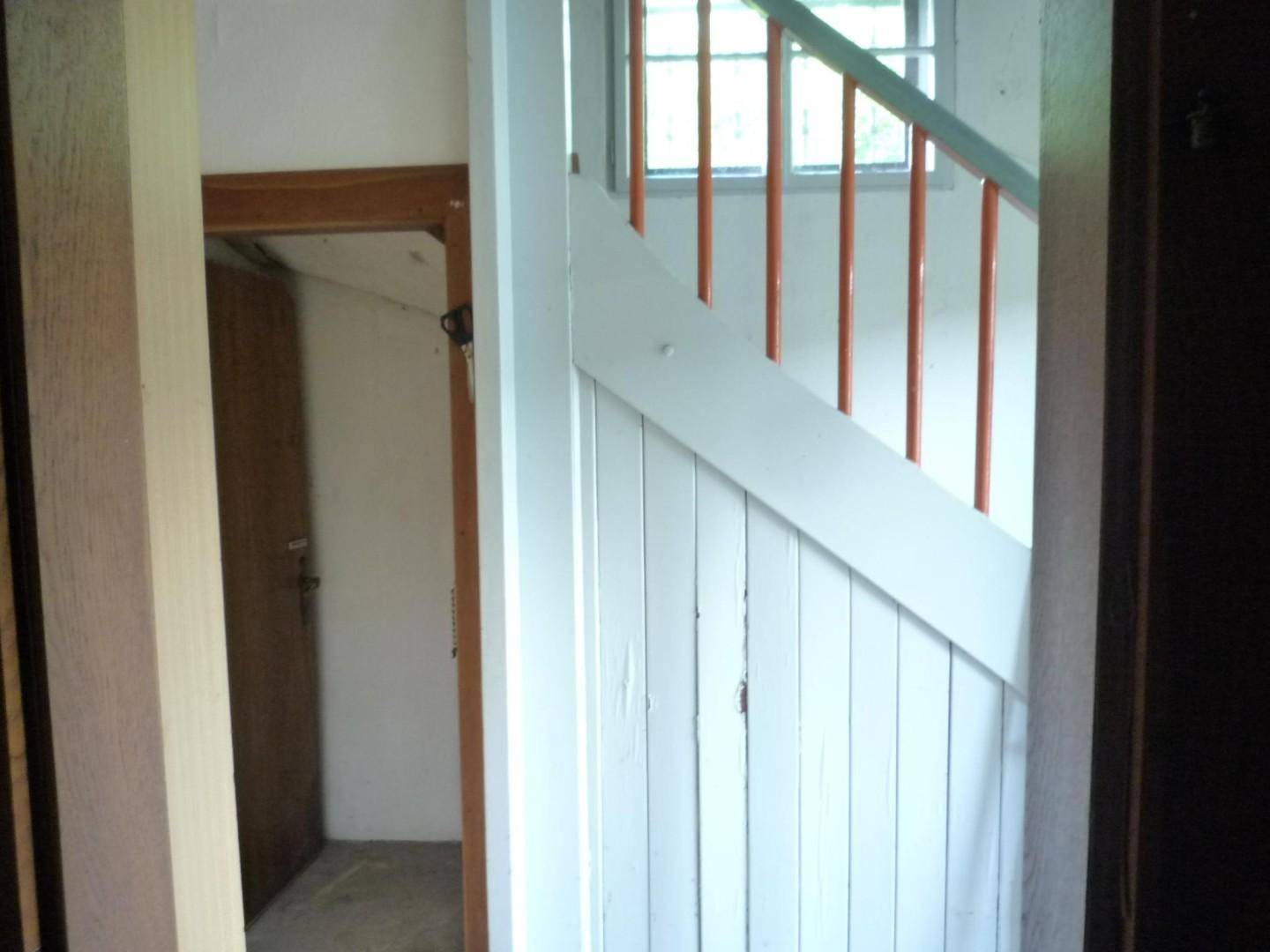 Holztreppe mit Geländer und Fenster, die zu einem oberen Stockwerk führt.