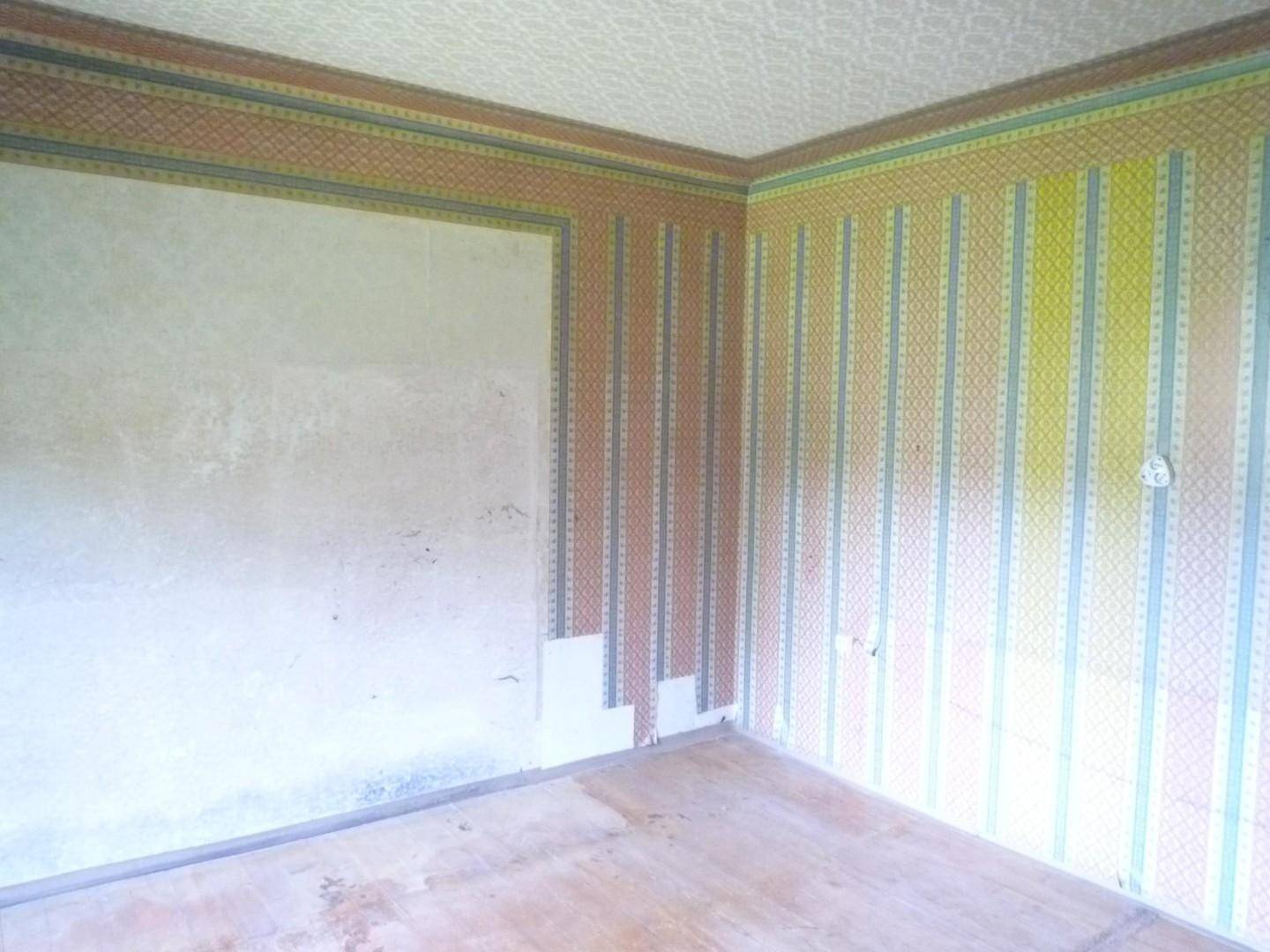Renovierungsbedürftiger Raum mit alter gestreifter Tapete und abgenutztem Holzboden.