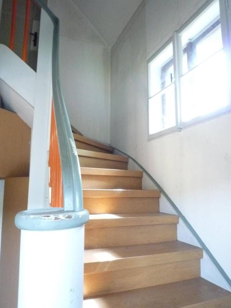 Helle Holztreppe mit geschwungenem Geländer und Fenster, das viel Tageslicht hereinlässt.
