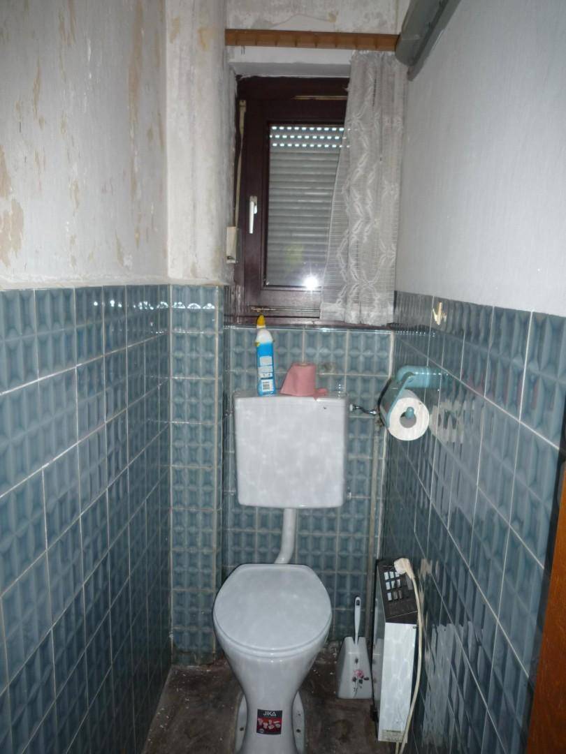 Kleines WC mit blauen Fliesen, Toilette und einem Fenster für natürliche Belüftung.