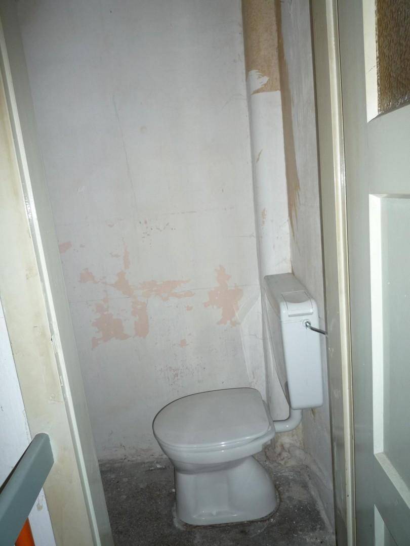 Kleines WC mit Toilette und weiß gestrichenen Wänden, bereit für eine Renovierung.