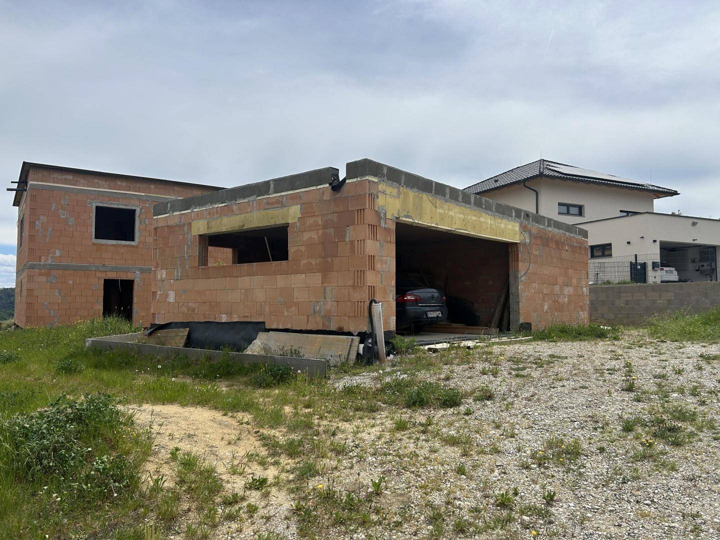 Rohbau eines Hauses mit integrierter Garage auf einem grünen Grundstück.