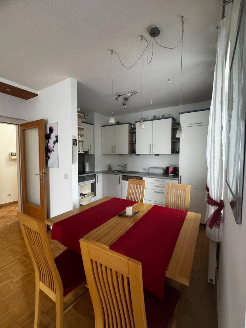 Offener Essbereich mit Holztisch und Stühlen, angrenzend an eine helle Einbauküche.
