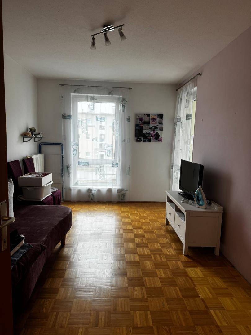 Gemütliches Wohnzimmer mit Parkettboden, einem Sofa und einem Fenster für natürliches Licht.