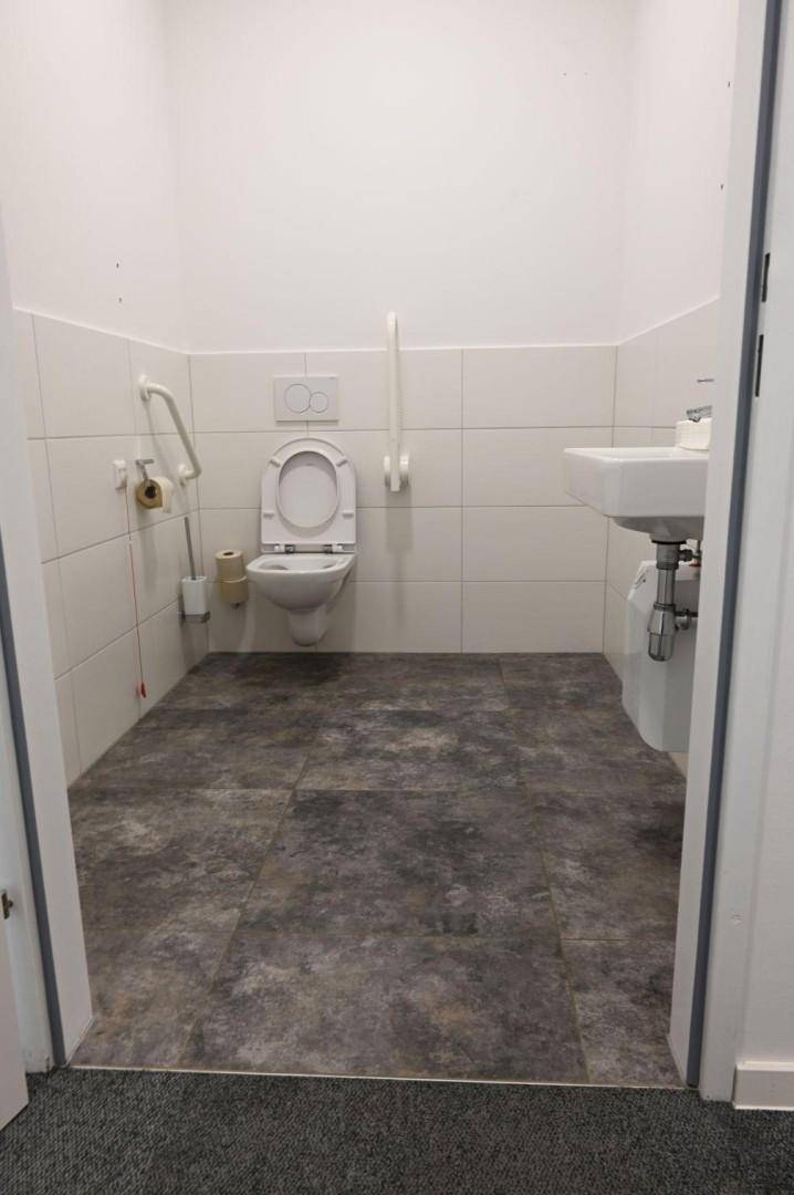 Barrierefreier Toilettenraum mit Haltegriffen, wandhängendem WC und Waschbecken, ideal für Rollstuhlfahrer.