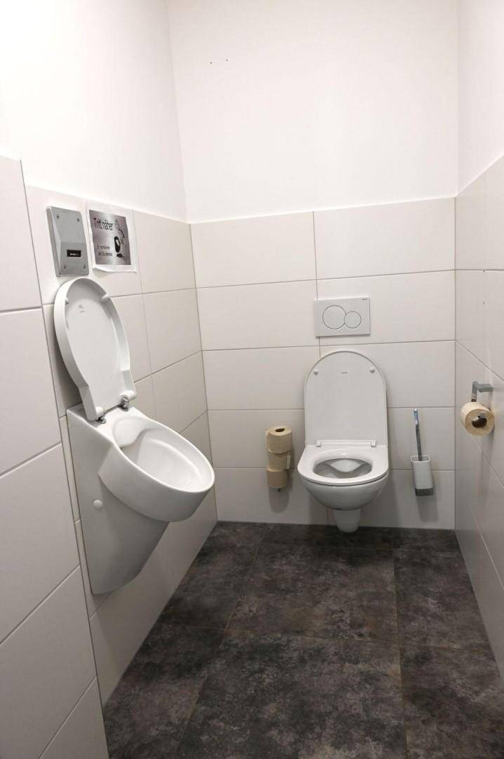 Toilettenraum mit wandhängendem WC, Urinal und gefliesten Wänden und Boden in neutralen Farben.