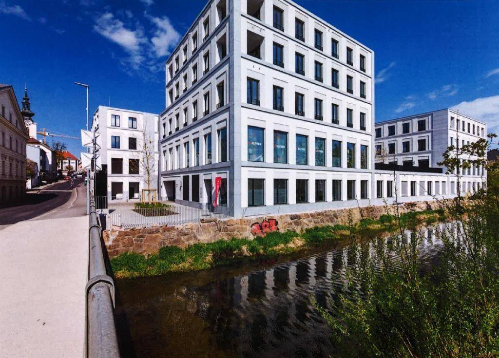 Moderne Bürogebäude am Flussufer unter blauem Himmel, mit zeitgenössischer Architektur und großen Fenstern.