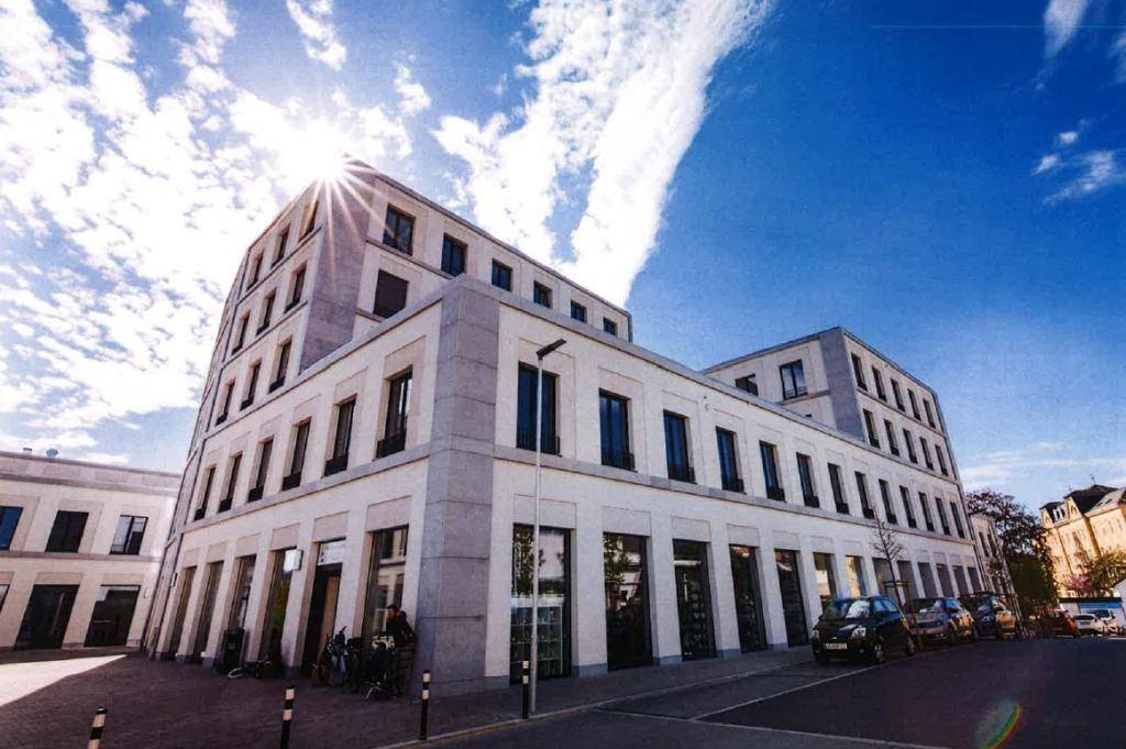 Modernes Geschäftsgebäude mit großen Schaufenstern im Erdgeschoss und heller Fassade unter strahlendem Himmel.