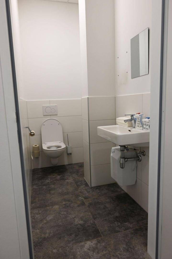 Kleiner Toilettenraum mit wandhängendem WC, Waschbecken und dunklen Fliesen auf dem Boden.