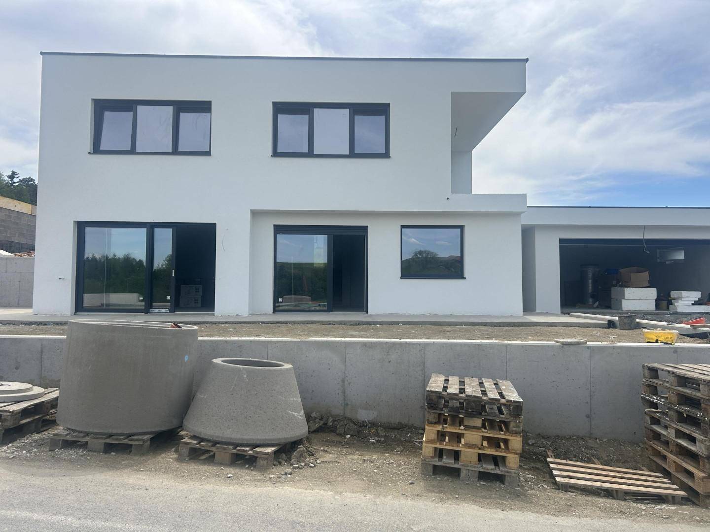 Vorderansicht eines modernen Neubaus mit weißer Fassade, großen Glasfronten und offenem Garagenbereich.