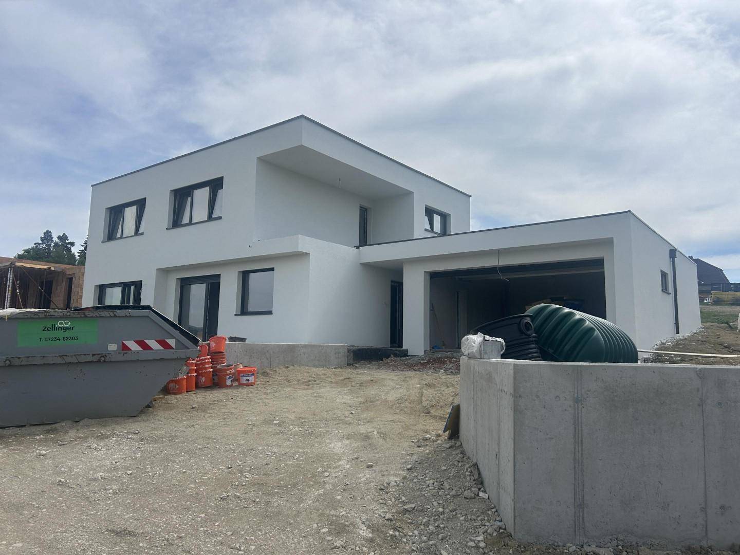 Modernes Einfamilienhaus im Bau mit weiß verputzter Fassade, großen Fenstern und integrierter Garage.