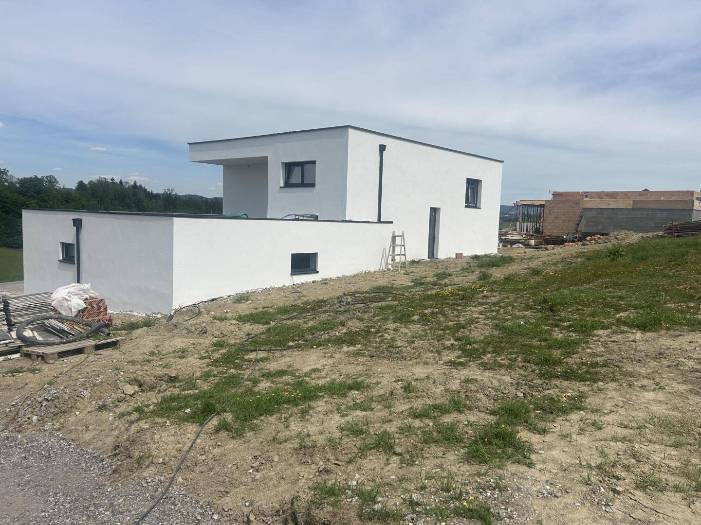 Seitenansicht eines modernen Neubaus mit weißer Fassade auf einem leicht abfallenden Grundstück.