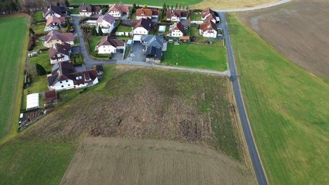 Luftaufnahme einer ländlichen Wohnsiedlung umgeben von grünen Feldern und einer Landstraße.