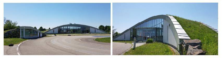 Modernes Gebäude mit geschwungenem Gründach und großer Glasfassade, umgeben von einer Zufahrtsstraße.