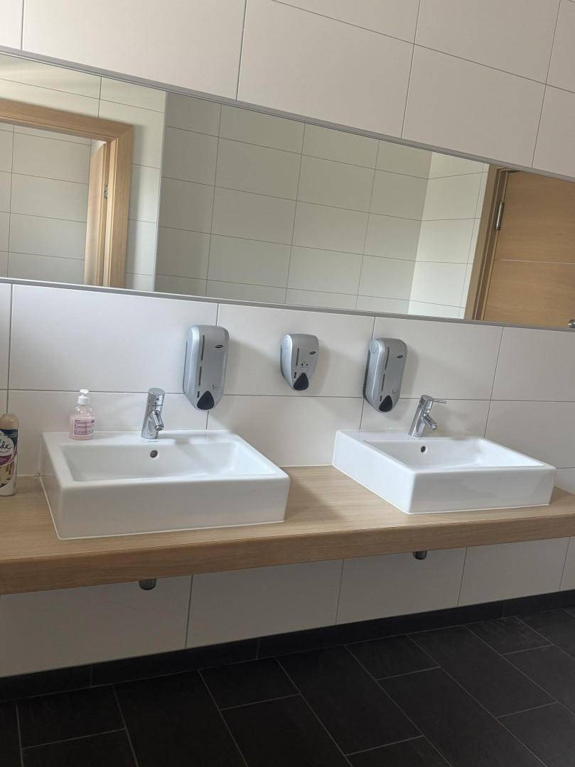 Modernes Badezimmer mit zwei rechteckigen Waschbecken, großem Spiegel und hellen Fliesen an Wänden und Boden.
