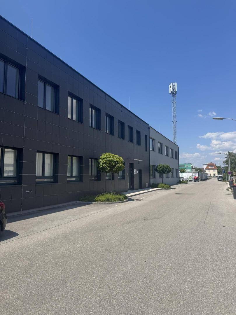 Seitenansicht des modernen Geschäftsgebäudes mit einer Straße und einem Mobilfunkmast im Hintergrund.