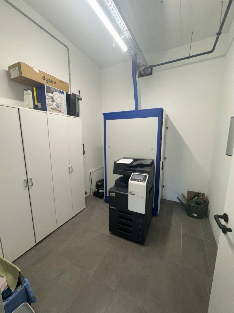 Funktionsraum mit großem Kopierer, weißen Schränken und sichtbaren Leitungen an der Decke, dient als Abstellraum.