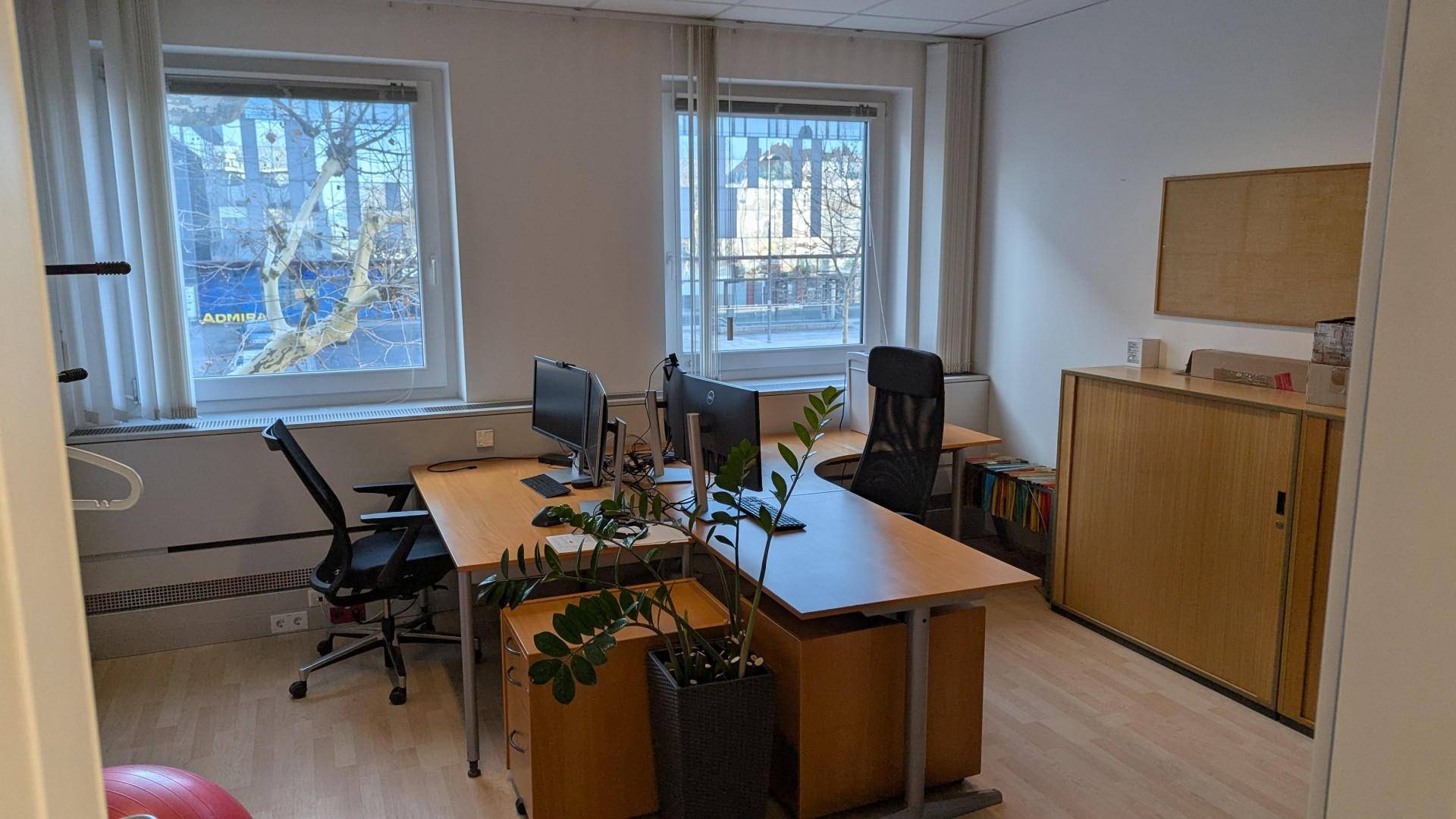 Büro mit zwei Arbeitsplätzen, Holzmöbeln und Fenstern mit Blick auf die Umgebung.