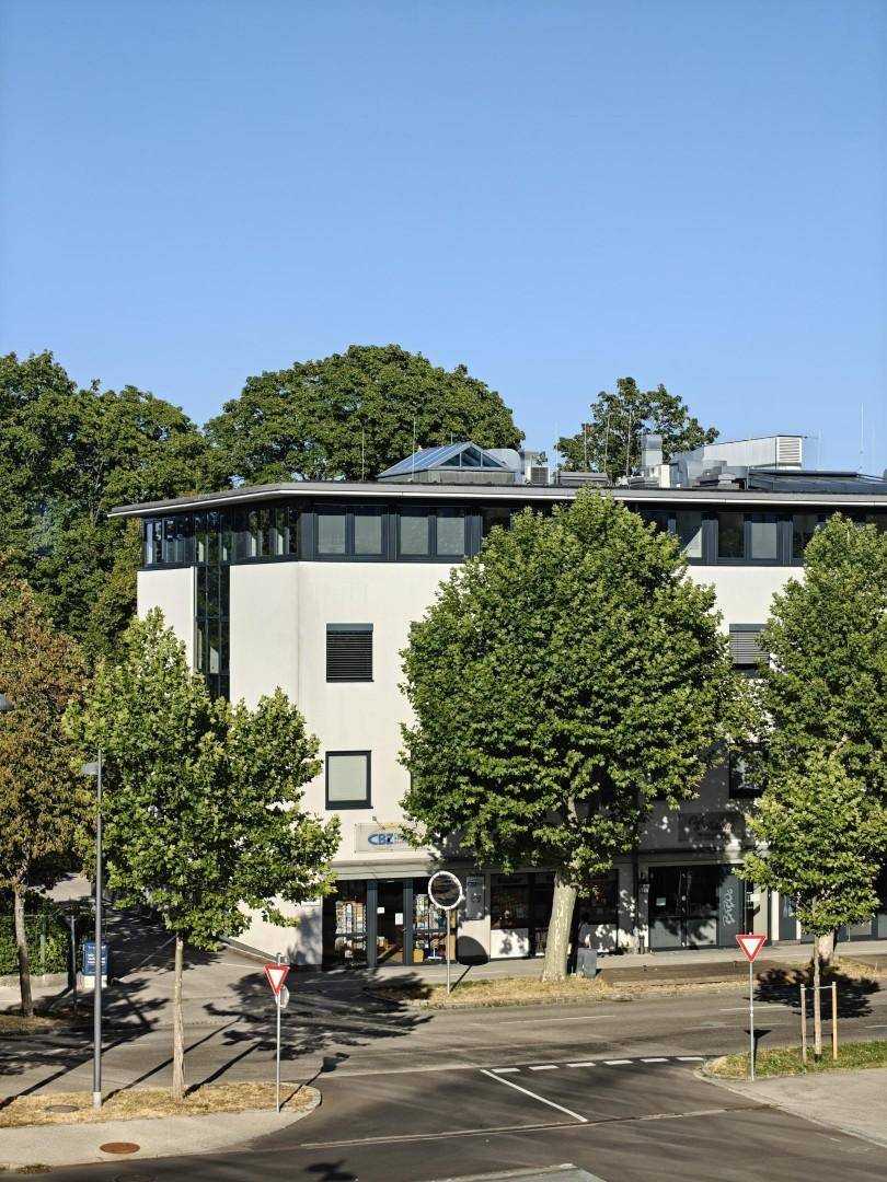 Ansicht des modernen Bürogebäudes mit großen Fenstern und umliegenden Bäumen unter blauem Himmel.