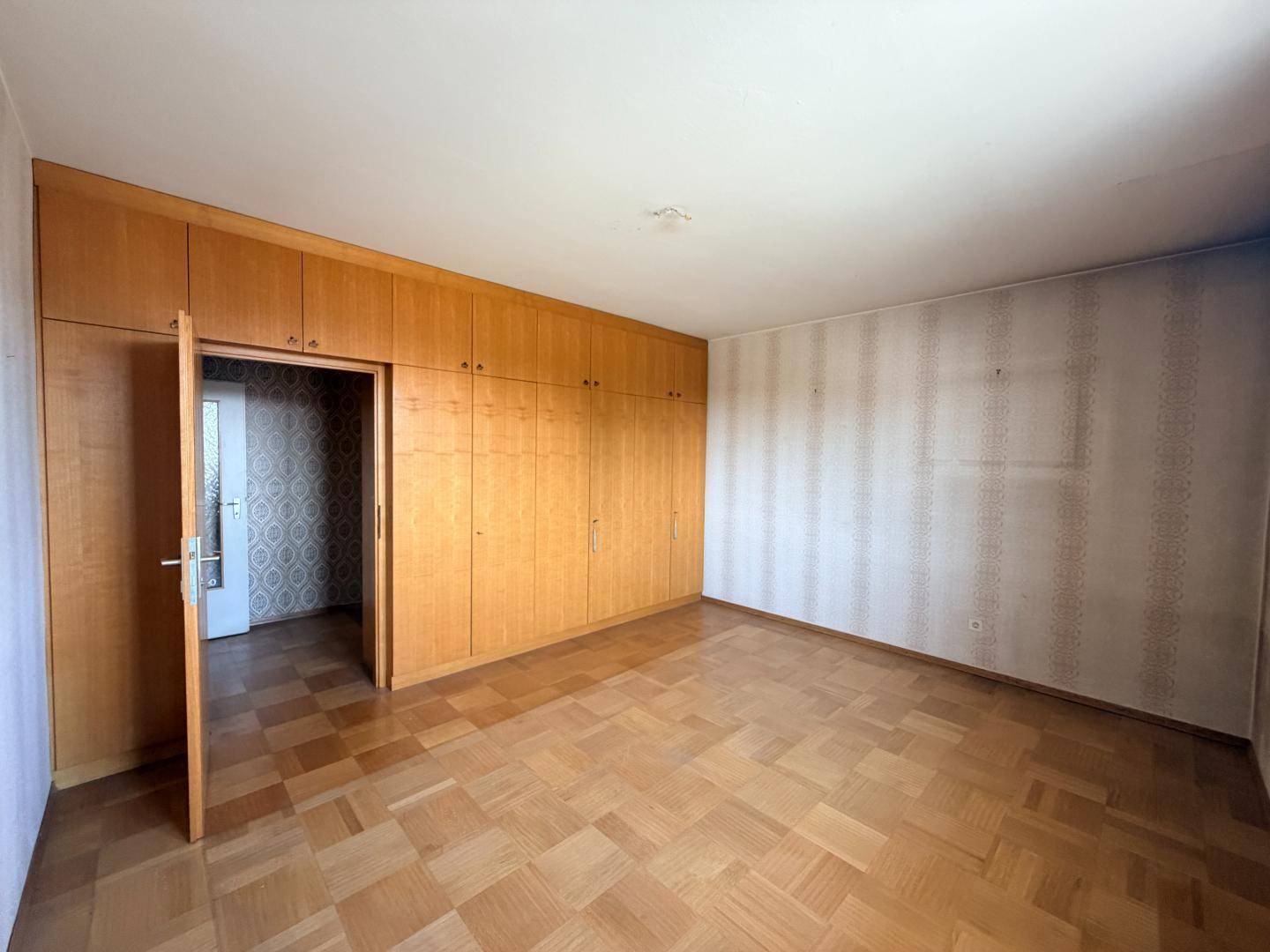 Geräumiges Schlafzimmer mit Einbauschränken, Parkettboden und gemusterter Tapete.