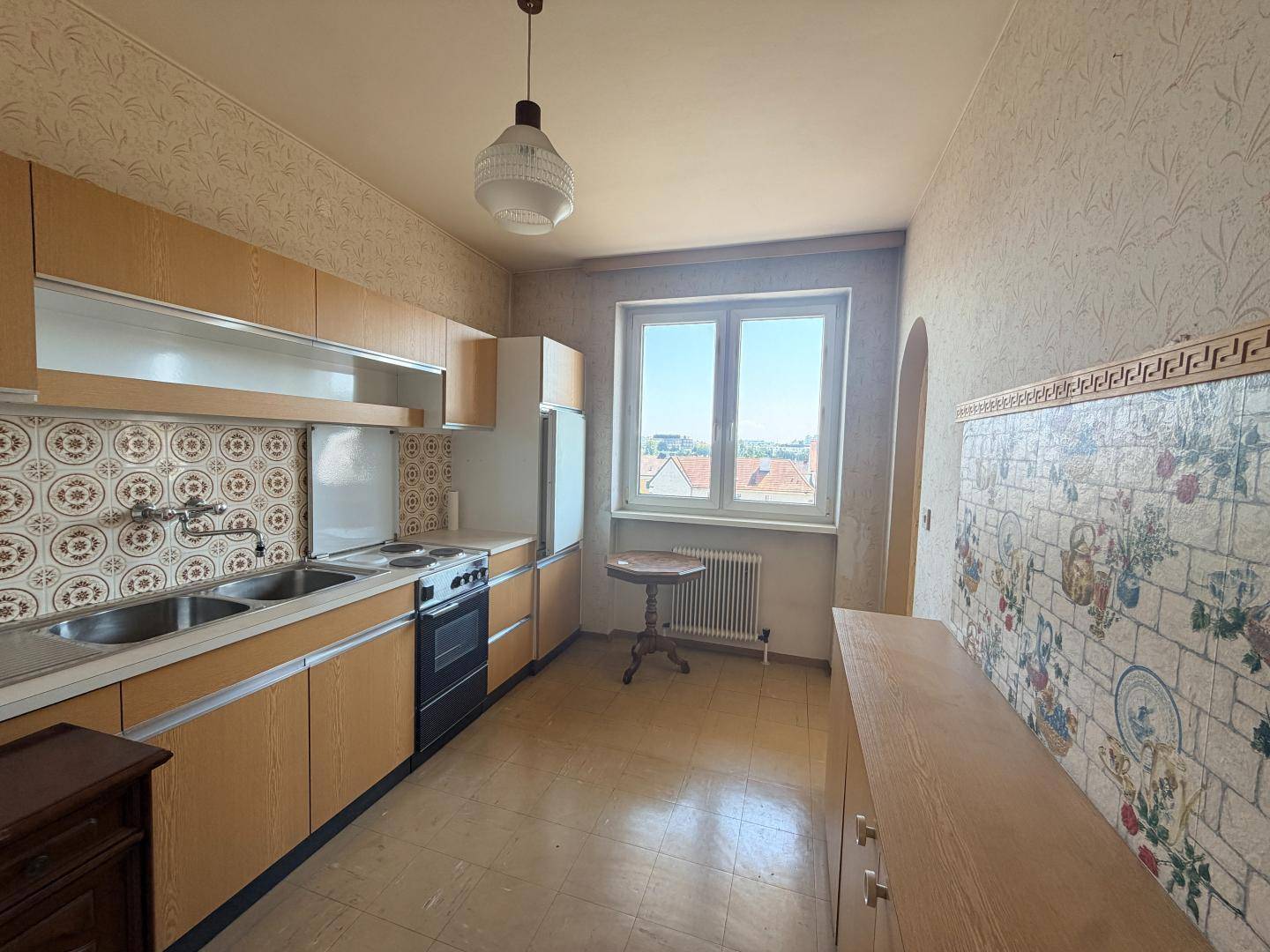 Küche im 80er-Jahre-Stil mit Einbauküche, Elektroherd und Fenster mit Ausblick.