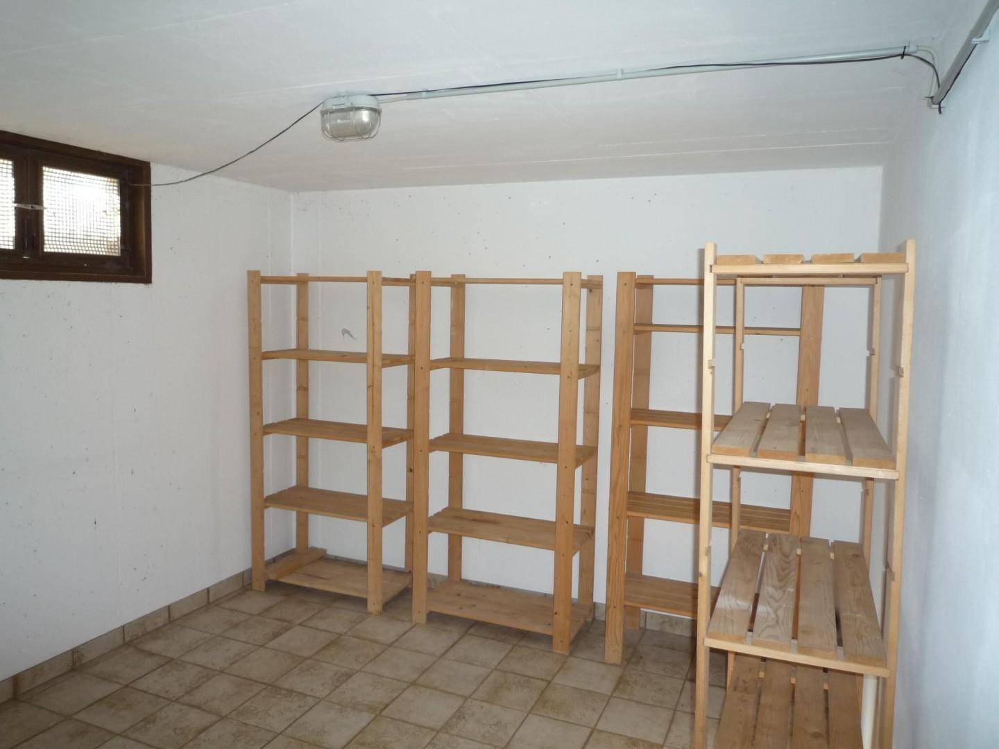 Geräumiger Abstellraum im Keller mit mehreren Holzregalen und einem kleinen Fenster.