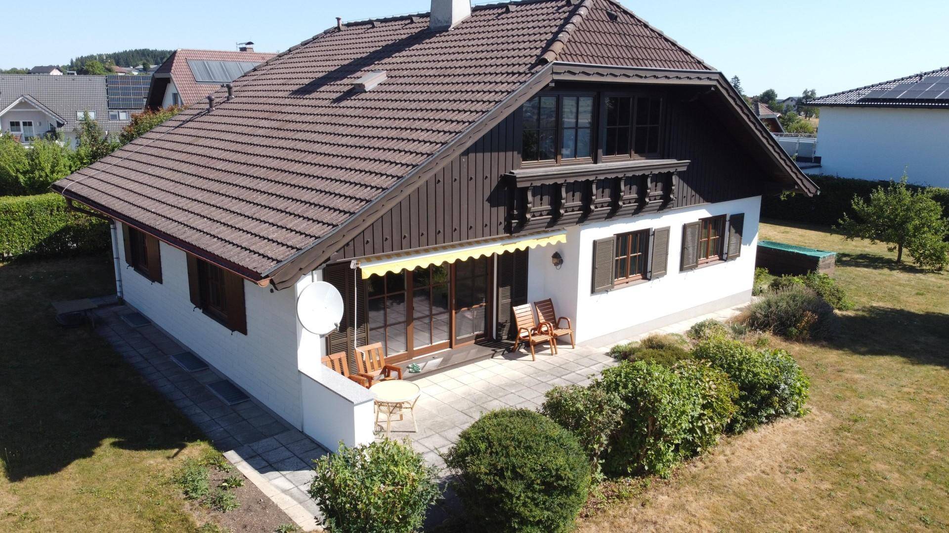 Seitliche Ansicht des Hauses mit einer gepflasterten Terrasse, Gartenmöbeln und einem weitläufigen Rasenbereich.