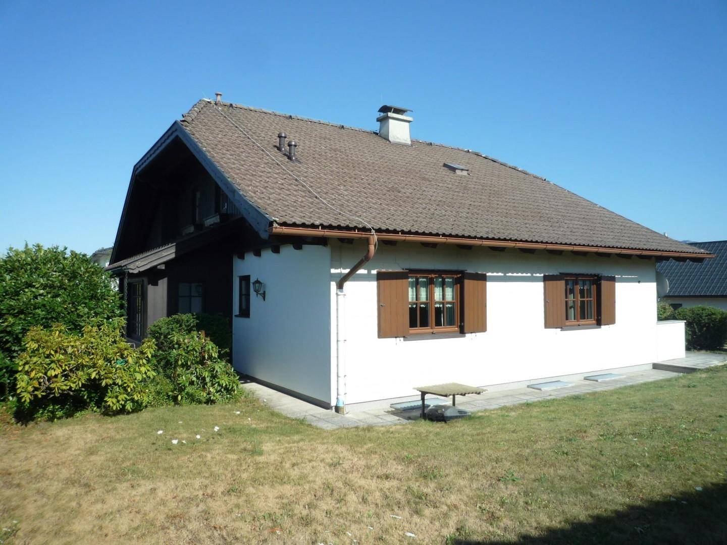 Einfamilienhaus mit weißer Fassade, braunem Ziegeldach und grüner Rasenfläche.
