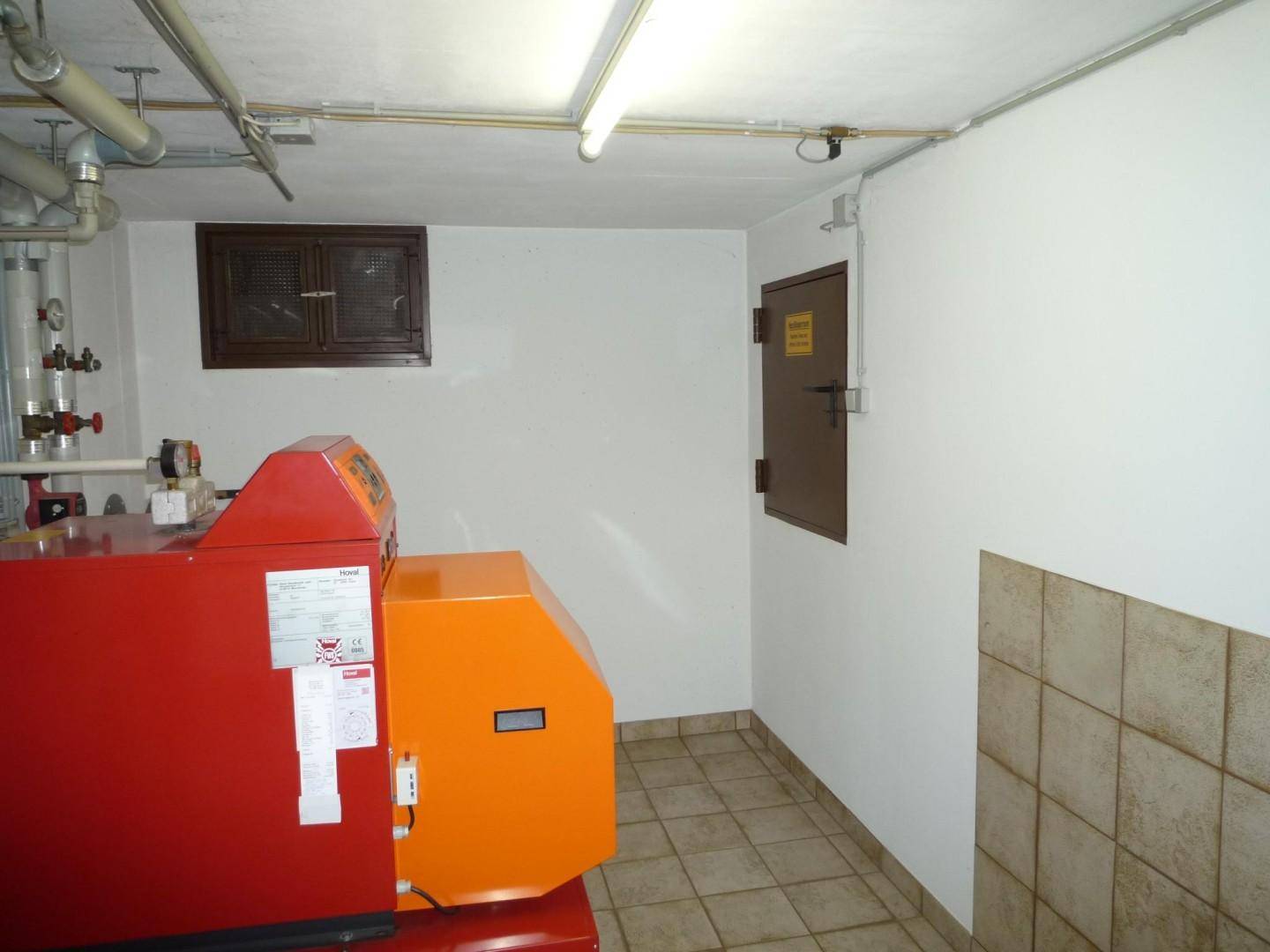 Heizungsraum mit großem Heizkessel, sichtbaren Rohren und Fliesenboden.
