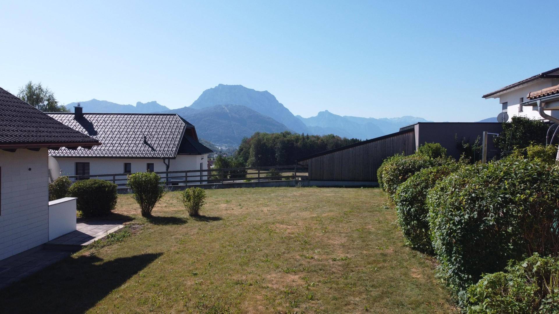 Großer, sonniger Garten mit Rasenfläche und einem beeindruckenden Blick auf die umliegende Berglandschaft.