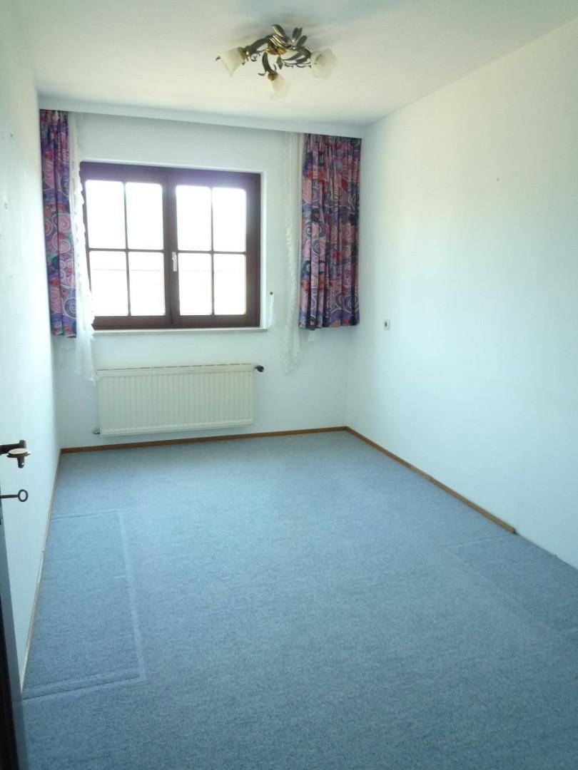 Schlichtes Schlafzimmer mit Teppichboden, weiß gestrichenen Wänden und einem Fenster mit Heizkörper darunter.
