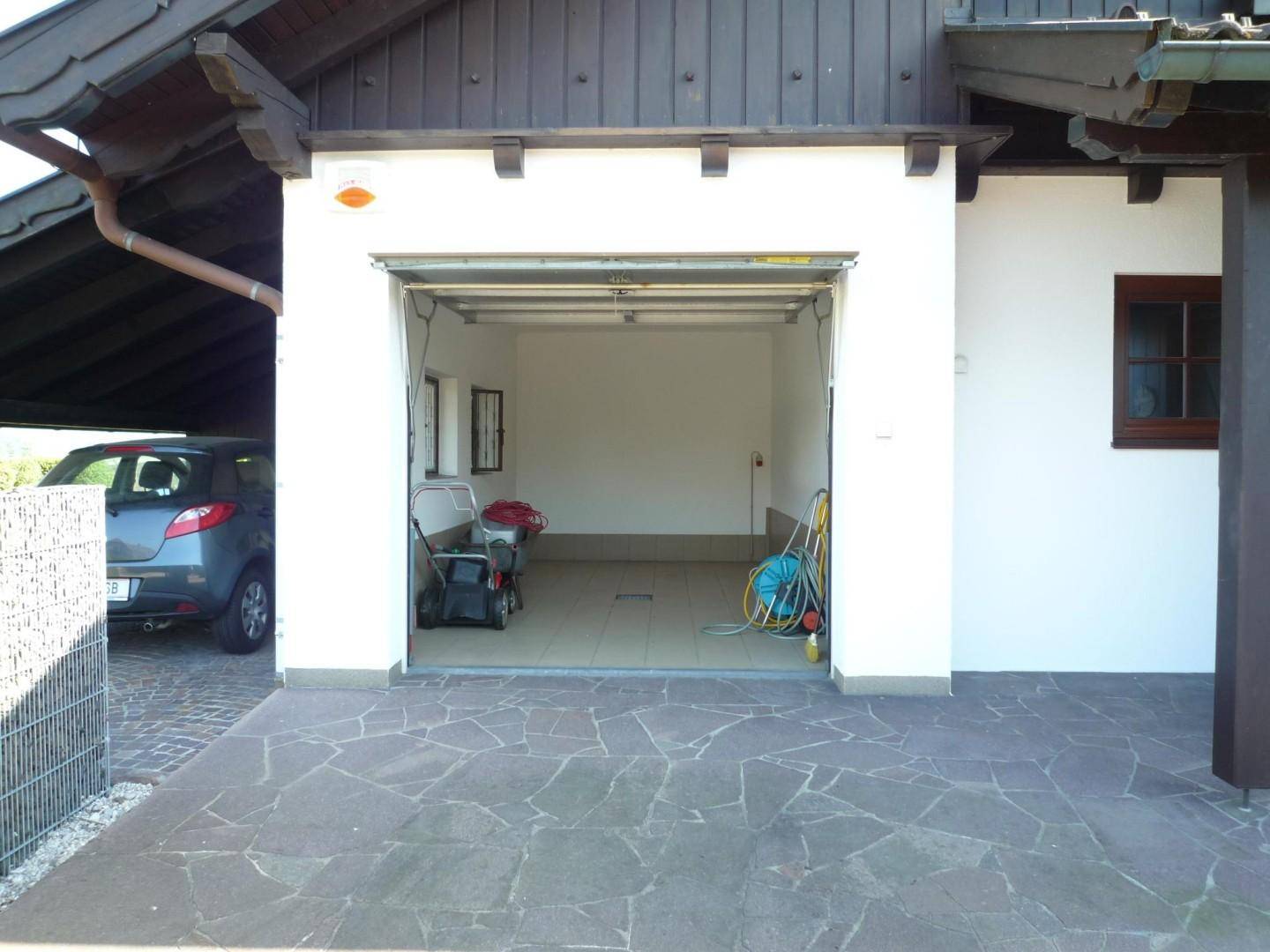 Offene Garage mit Werkzeugen und Gartengeräten, daneben ein Carport mit geparktem Auto.