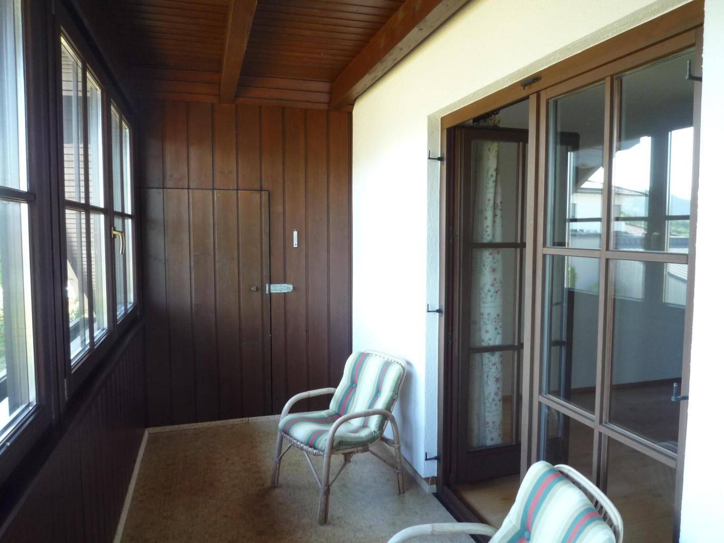 Verglaster Wintergarten oder Loggia mit Holzverkleidung, Sitzgelegenheiten und weitem Ausblick.