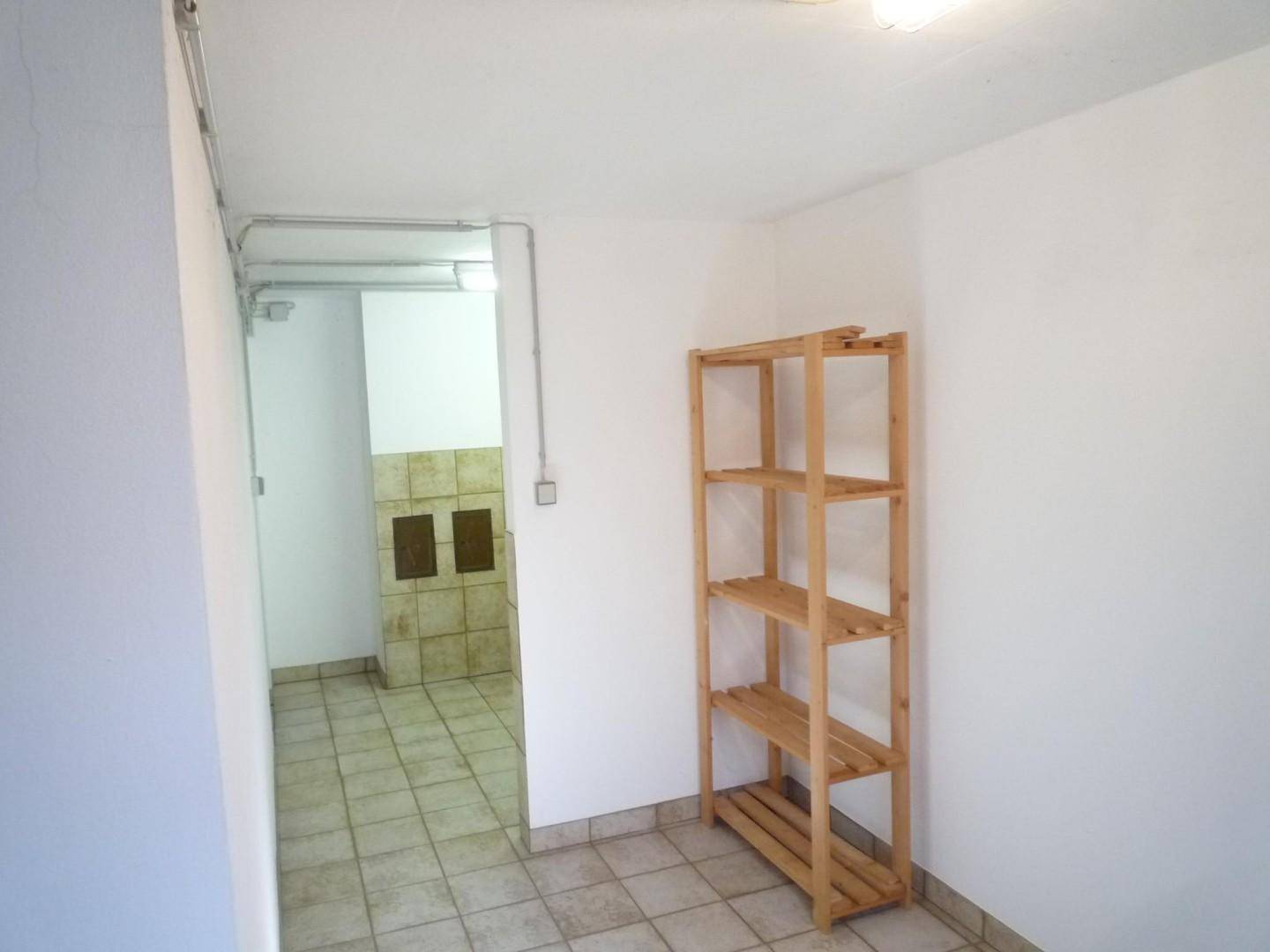 Einfacher Abstellraum mit Fliesenboden und einem Holzregal, ideal für Lagerzwecke.