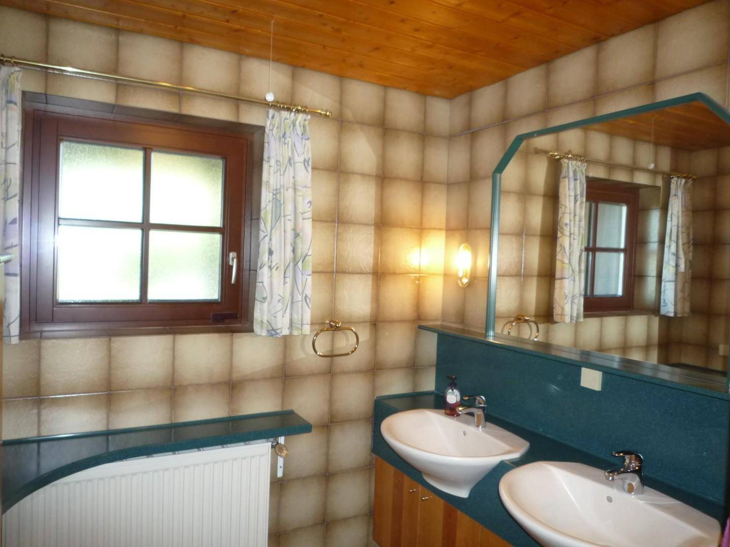 Badezimmer im Stil der 80er Jahre mit doppelten Waschbecken, braunen Fliesen und Holzdecke.