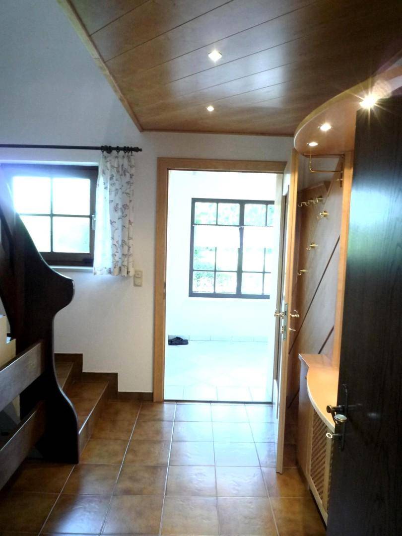 Eingangsbereich mit Fliesenboden, Holzdecke und einer Garderobe, die zu weiteren Räumen führt.