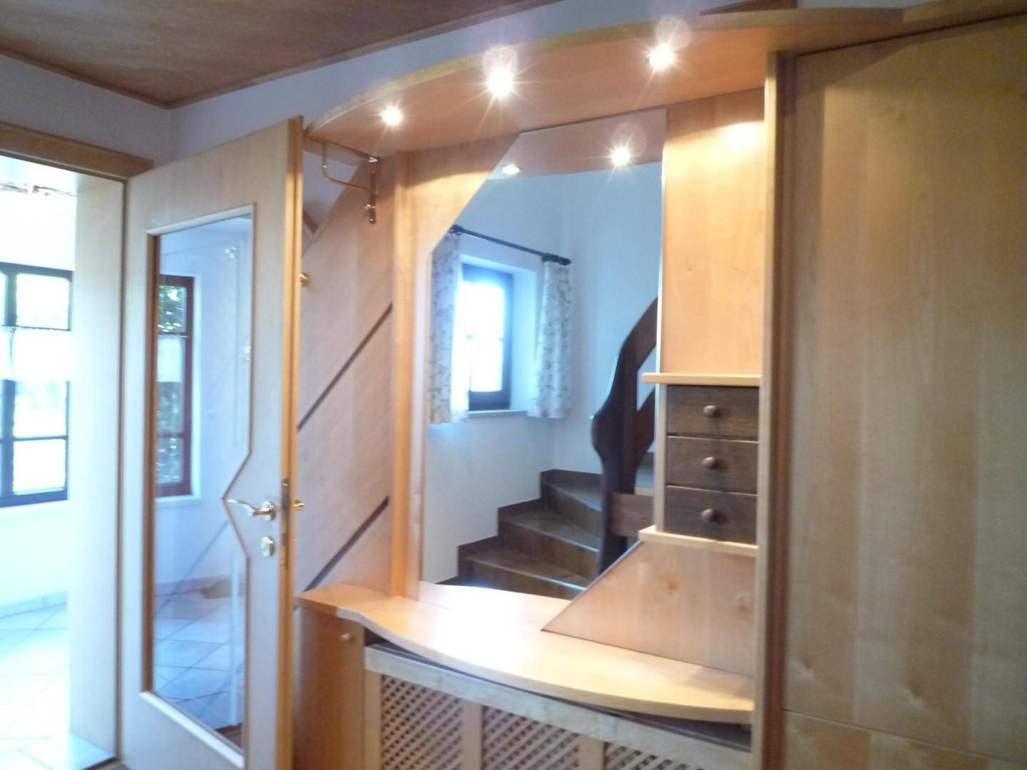 Heller Eingangsbereich mit maßgefertigten Holzmöbeln, integrierter Beleuchtung und einer Holztreppe zum Obergeschoss.