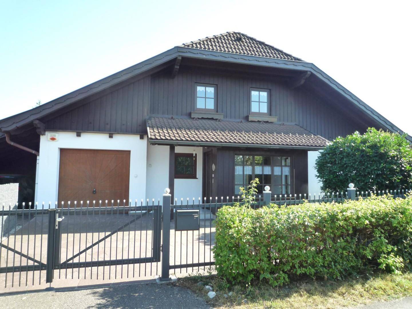 Vorderansicht des Hauses mit Garagentor, Einfahrt und einem gepflegten Vorgarten hinter dem Zaun.