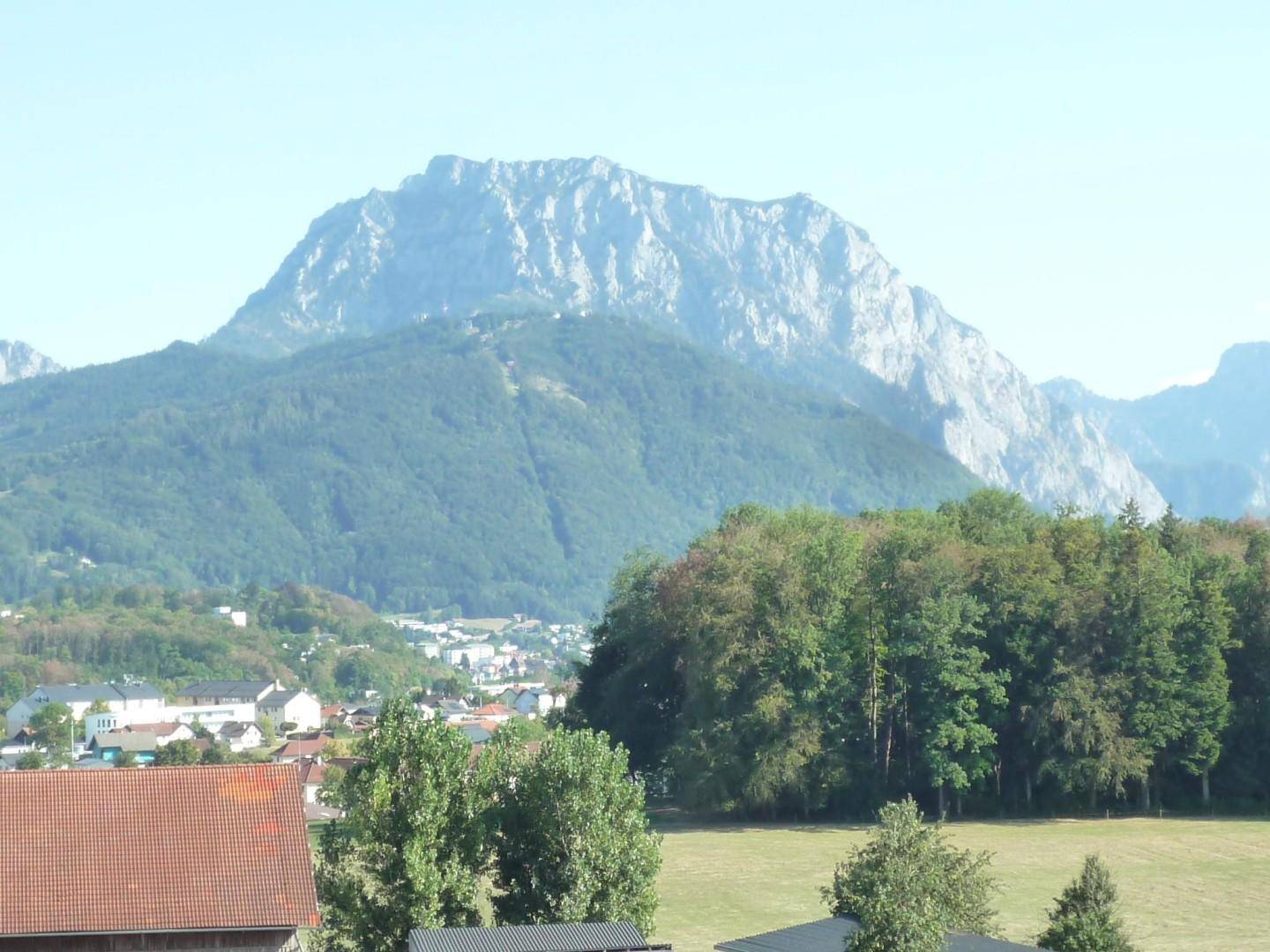 Panoramablick auf die majestätische Bergkette und die darunterliegende grüne Landschaft mit Siedlung.