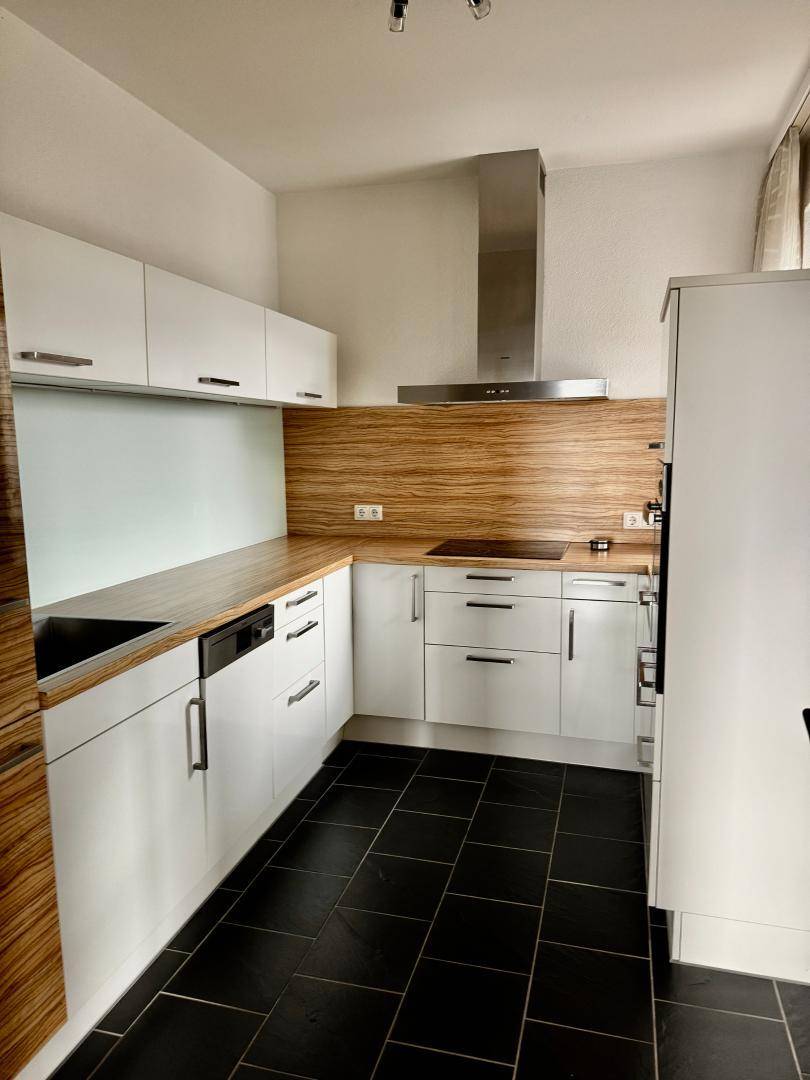 Moderne Küche mit weißen Fronten, Holzakzenten und dunklen Fliesenboden.