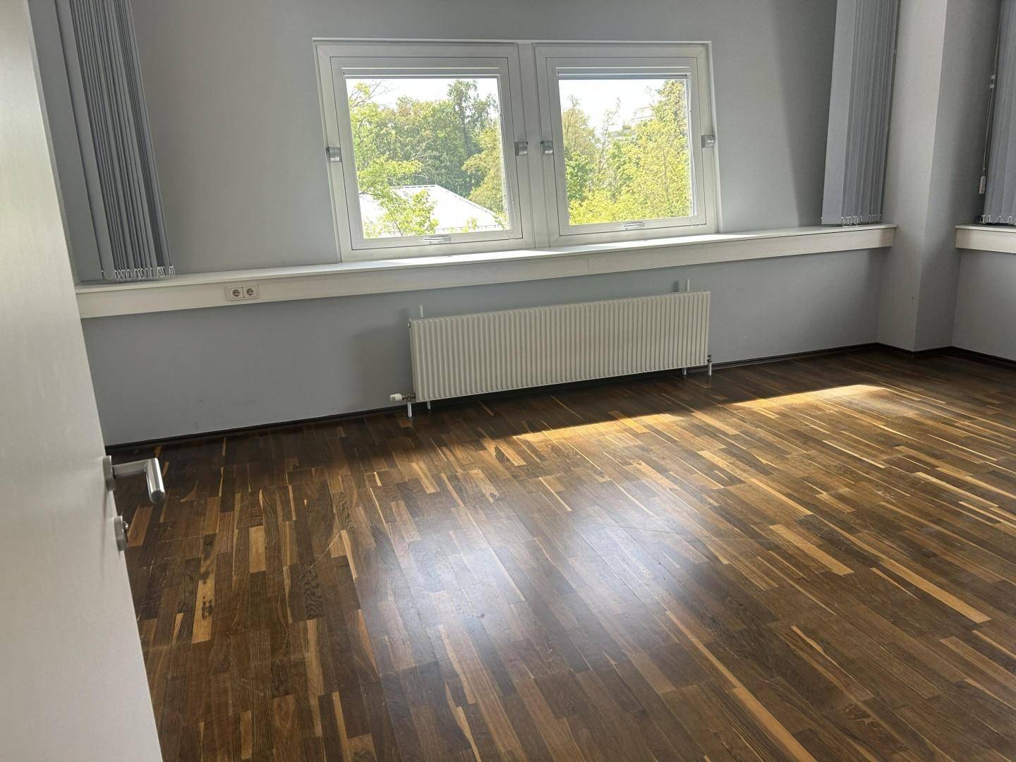Helles Büro mit dunklem Parkettboden, grauen Wänden und Blick ins Grüne.