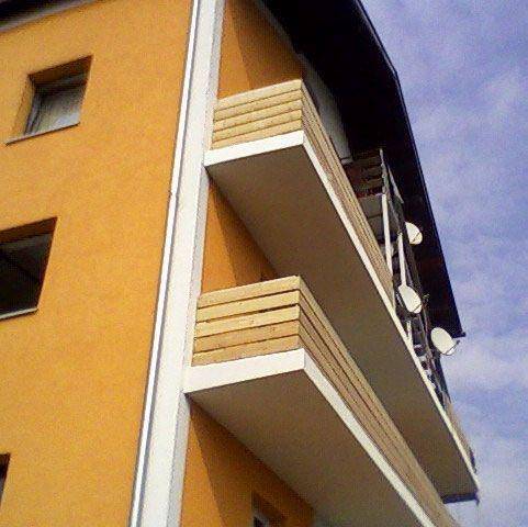 Nahaufnahme einer Gebäudeecke mit orangefarbener Fassade und zwei Balkonen mit Holzgeländern.
