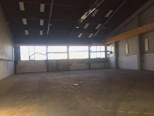 Leere Lagerhalle mit Betonboden, hohen Fenstern und einem Kran an der Decke.